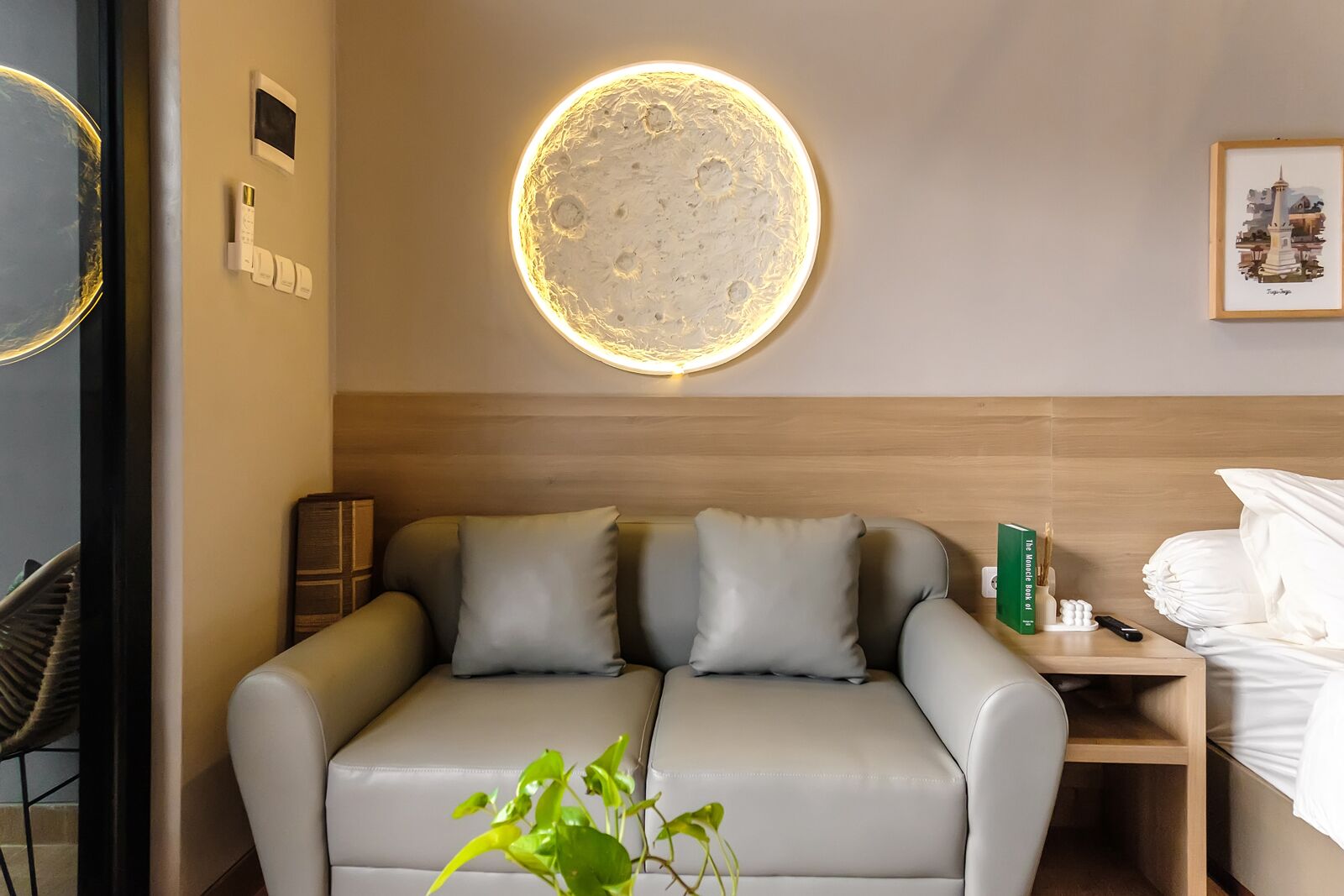 Ein modernes Hotelzimmer mit einer Couch, einem Nachttisch mit Fernbedienung, einem grünen Buch und einem gerahmten Bild an der Wand.