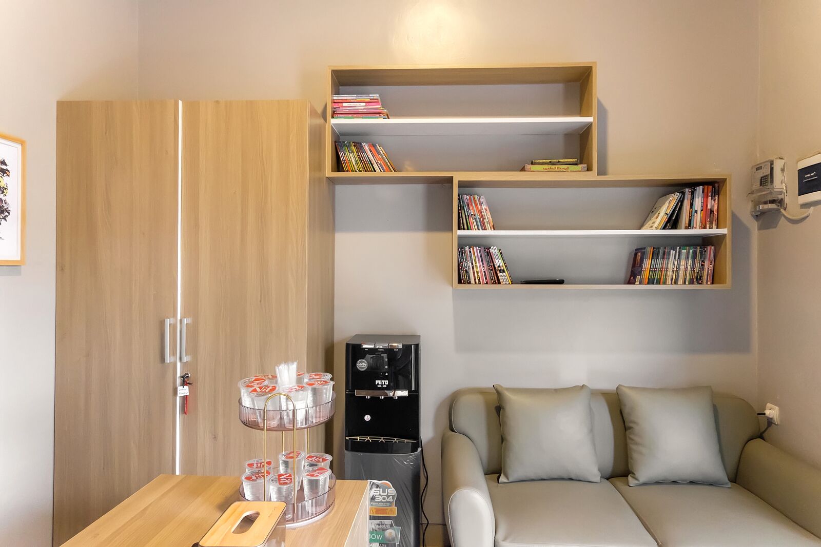 Un espace de vie compact comprenant un canapé, une machine à café, une bibliothèque et une armoire en bois.