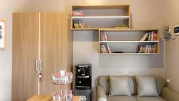 A compact living space with a sofa, a coffee machine, a bookshelf, and a wooden wardrobe.