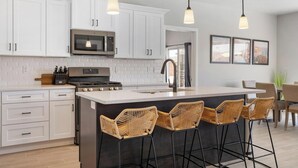 A modern kitchen with white cabinets, a stainless steel microwave, a gas stove, and a large island with bar stools. - Luxury 5BR Wellness Retreat w/ Private Pool, Hot Tub & Cold Plunge Near Zion (Hurricane)