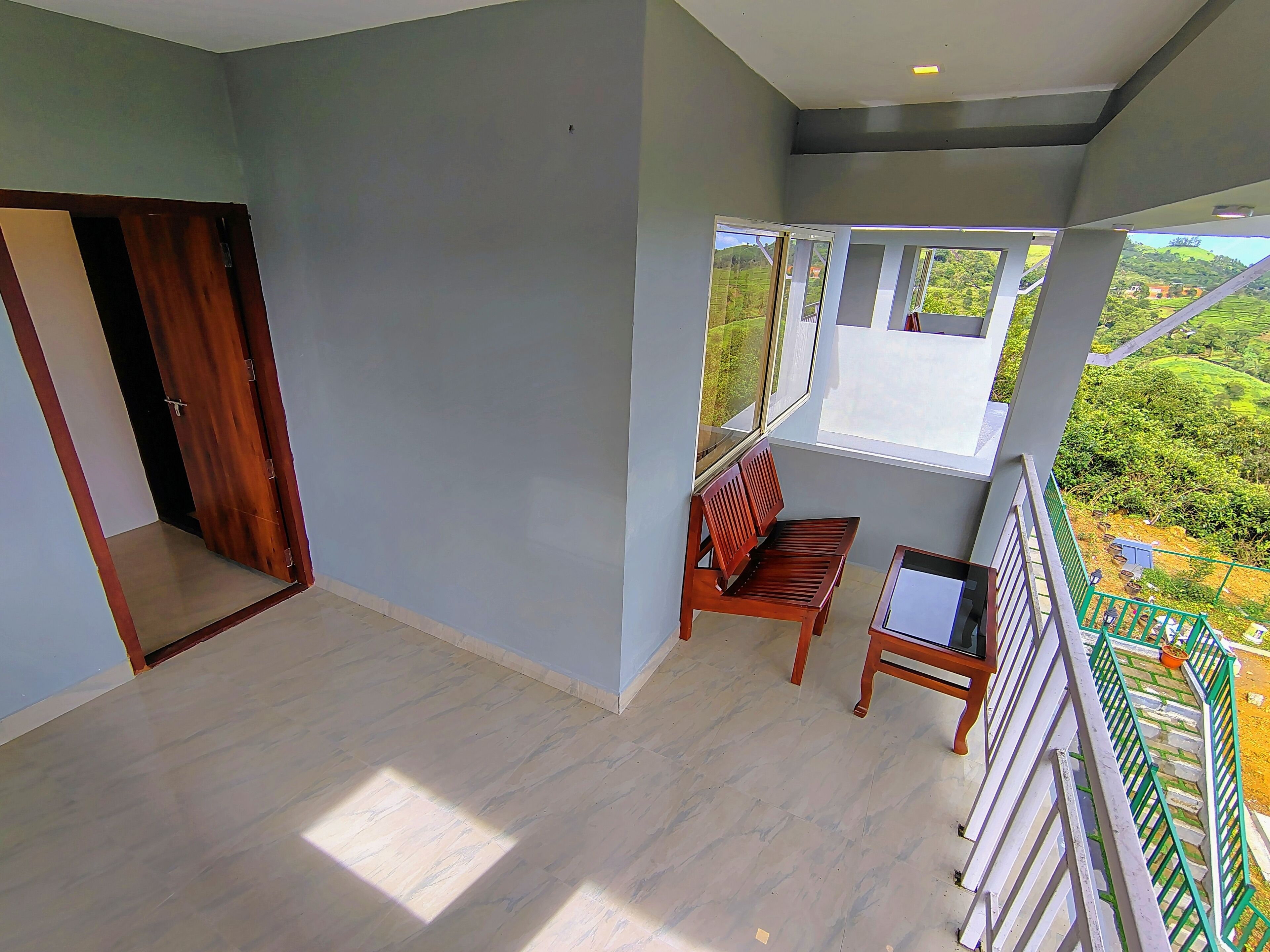 Un balcón con una silla de madera, una mesita y vistas al verdor.