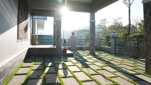 Een overdekt buitengebied met een stenen vloer en stukjes groen gras, een poort en uitzicht op het omliggende landschap.