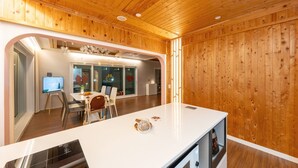 A modern kitchen with wooden paneling, a central island, and a dining area with chairs and a table. - Yeosu La Rosa Private Pool Villa Pension (Yeosu)