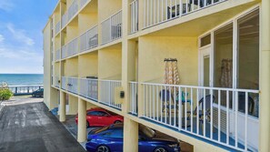 Un hotel su più piani con balconi, area piscina e auto parcheggiate davanti.
