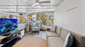 A living room with a large TV, a sofa, a coffee table, and a ceiling fan.