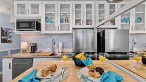 Een moderne keuken met witte kasten, roestvrijstalen apparatuur en een ontbijt met muffins en sinaasappelsap.