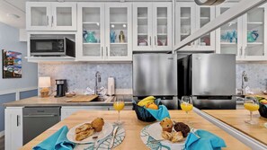 Une cuisine moderne avec des meubles blancs, des appareils en acier inoxydable et un coin petit-déjeuner avec des muffins et du jus d’orange.