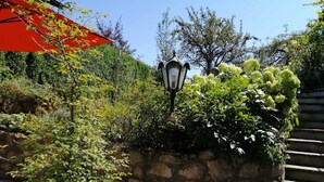 A stone wall with a lantern, surrounded by lush greenery and a red umbrella.