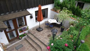 A stone patio with a table and chairs, a potted plant, and a window with curtains.