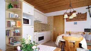 A compact kitchen with a microwave, oven, and wooden cabinets. There is a dining table with chairs and a vase of flowers on the table.