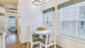 En matplats med ett vitt bord och stolar, en kristallkrona och stora fönster med persienner.
