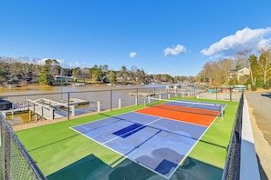 Una cancha de tenis con vistas a un lago y edificios al fondo.