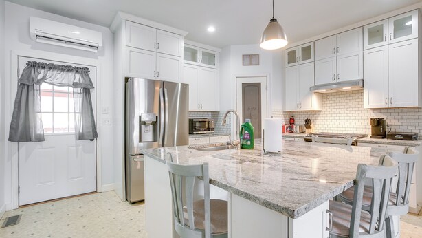 A modern kitchen with white cabinets, a stainless steel refrigerator, a granite countertop, and a built-in island with bar stools. - 4 Mi to Lake Logan: Hocking Hills Apartment (Logan)