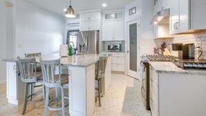 A modern kitchen with white cabinets, a central island with bar stools, a stainless steel refrigerator, and a gas stove. - 4 Mi to Lake Logan: Hocking Hills Apartment (Logan)