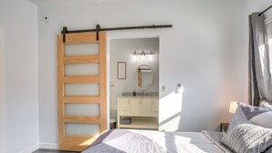 A bedroom with a bed, a wooden sliding door, a bathroom with a mirror and cabinets, and a window with curtains. - 4 Mi to Lake Logan: Hocking Hills Apartment (Logan)