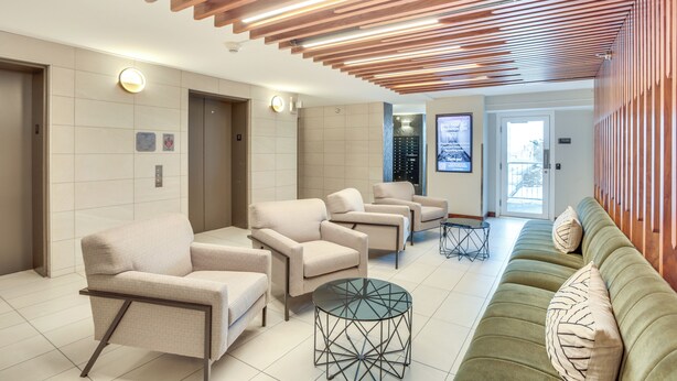 Eine moderne Lobby mit einem grünen Sofa, beigen Sessel und einem runden Glastisch.