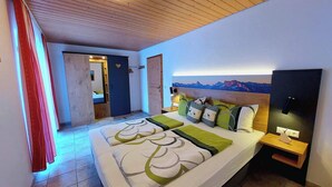 A bedroom with a bed, a nightstand, a wall-mounted lamp, a painting of mountains, and a wooden ceiling. - Ferienwohnung 6 Kehlstein für 1-2 Personen (Marktschellenberg)