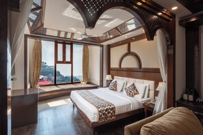 A spacious bedroom with a large bed, a sitting area with a view, and a ceiling fan. - The Solitaire Resort by Lawrence Hotels (Mussoorie)