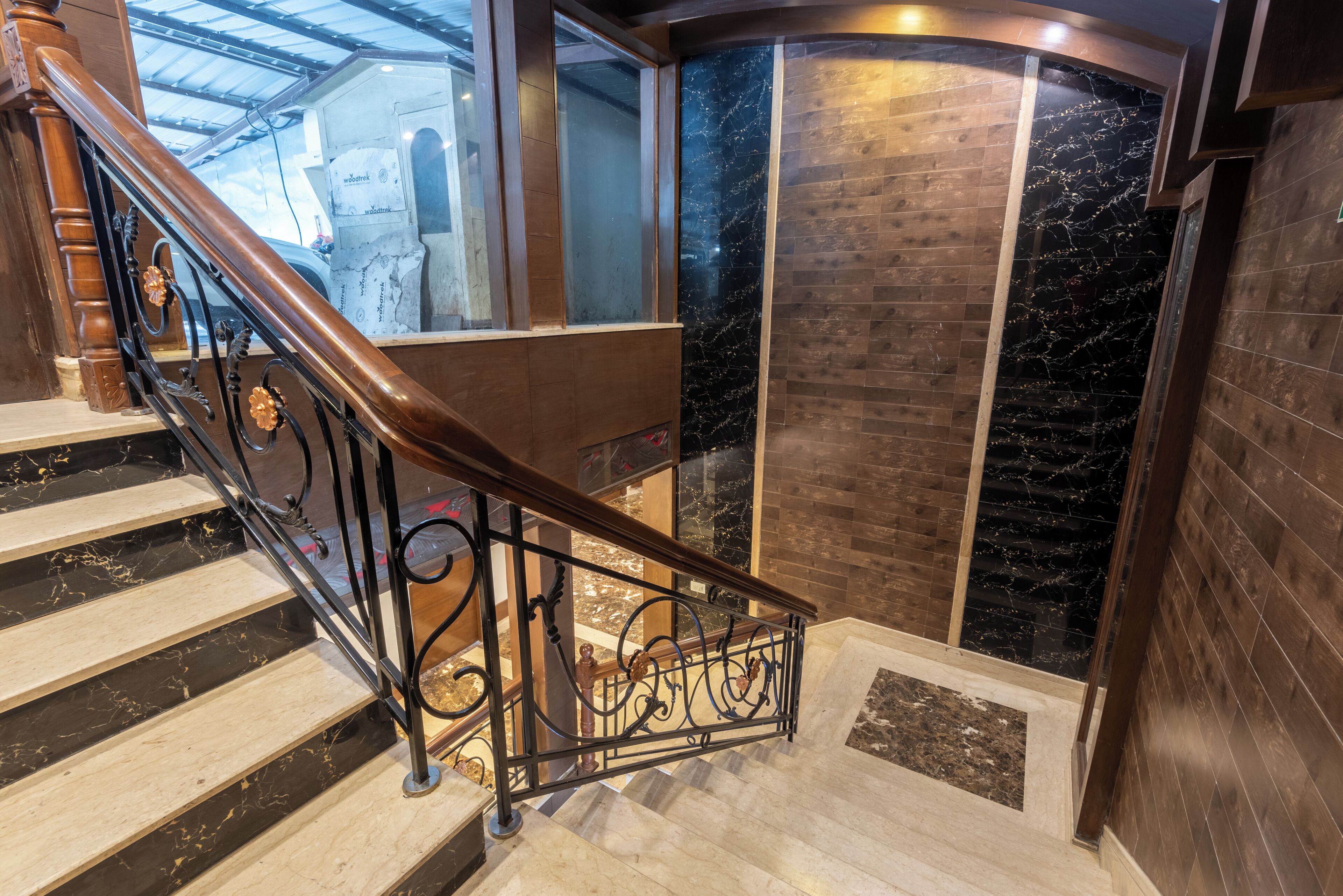 Un escalier doté d’une rampe en bois et de balustrades en métal noir, menant à un palier avec un mur en verre et un mur en marbre.