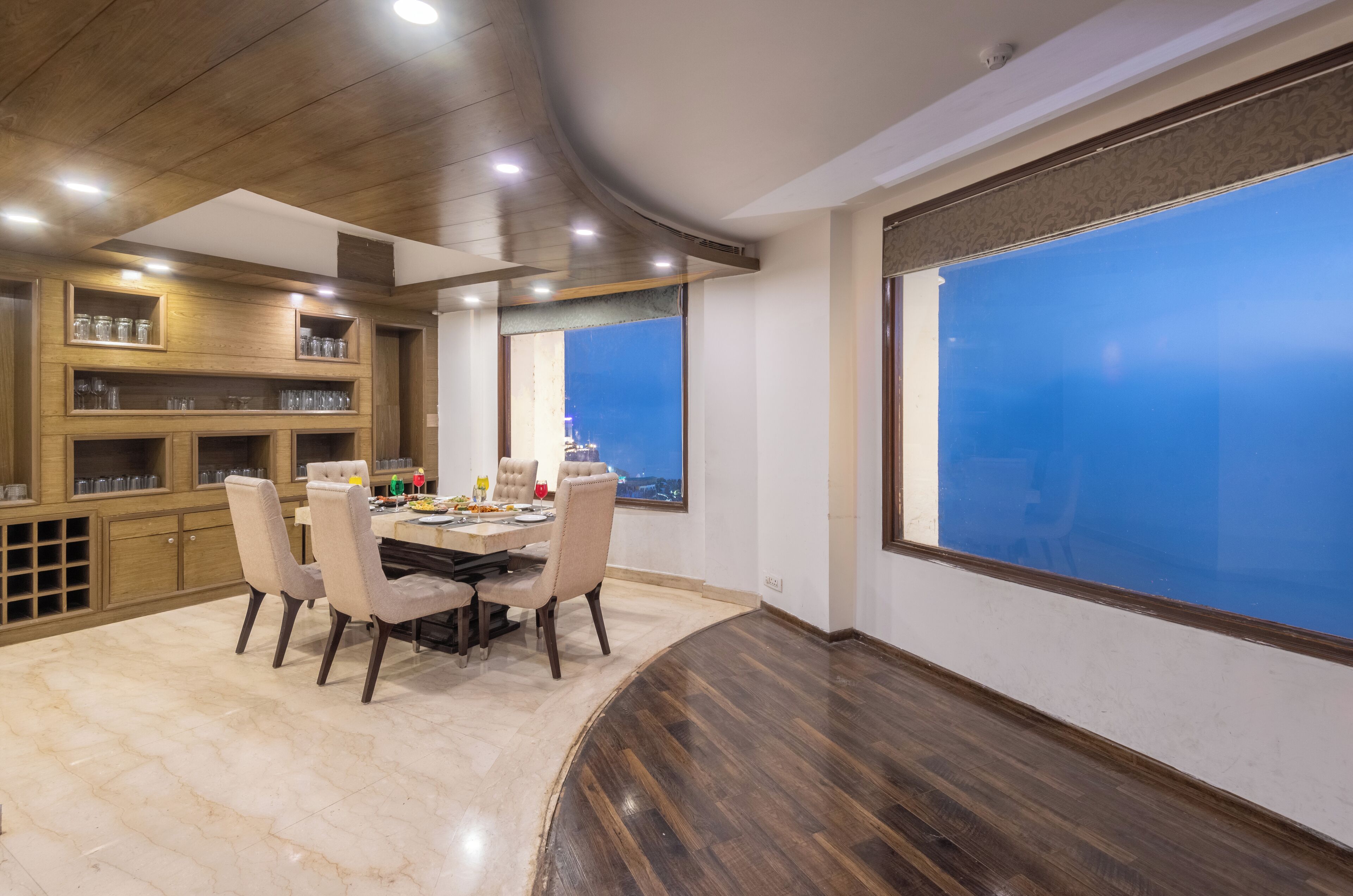 A dining area with a round table, chairs, and a view of the city through large windows.