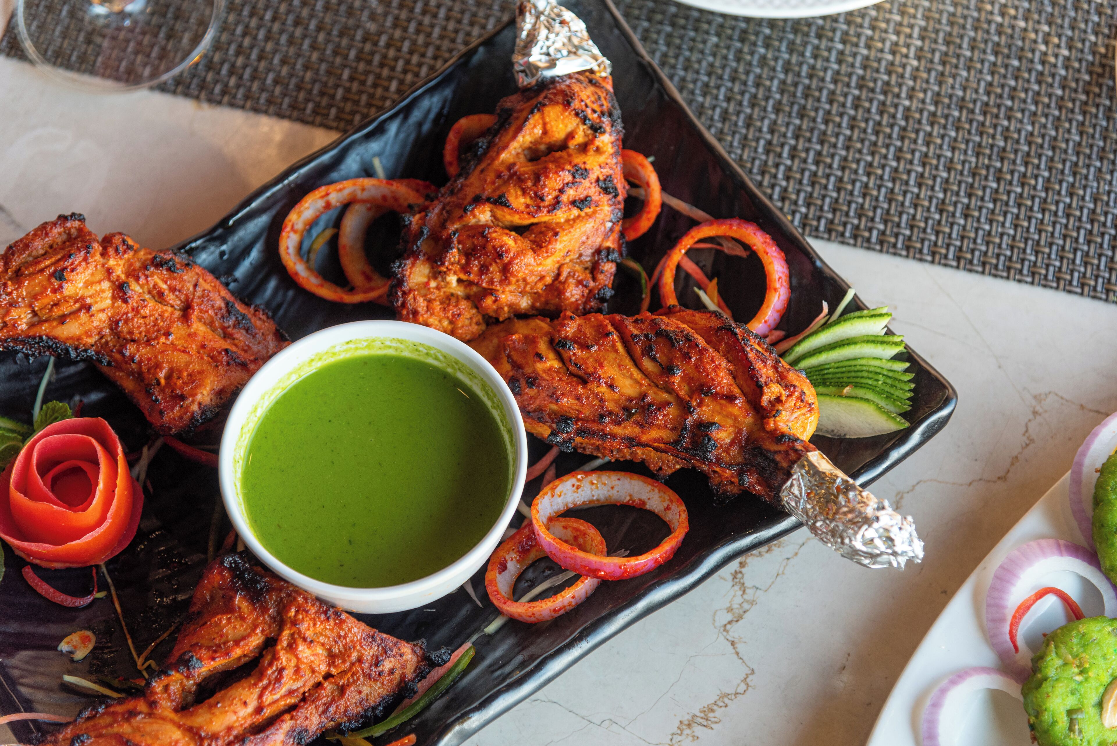 Un plato de pollo a la parrilla con aros de cebolla y salsa verde.