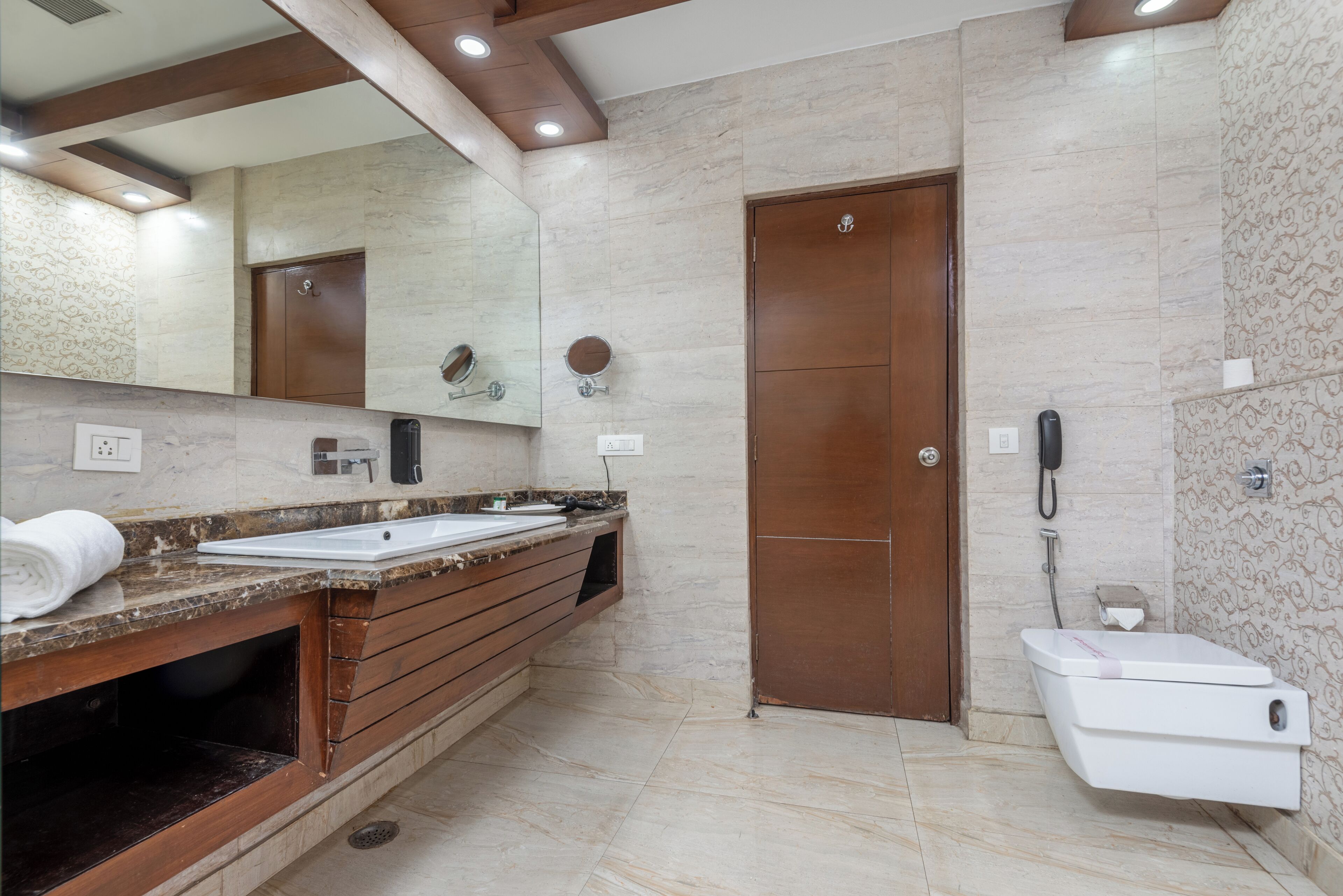 A modern bathroom with a marble vanity, a wooden door, and a toilet.