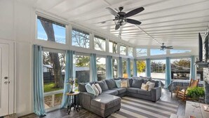 Ein Wintergarten mit einer großen Eckcouch, einem Holztisch und einem Deckenventilator.