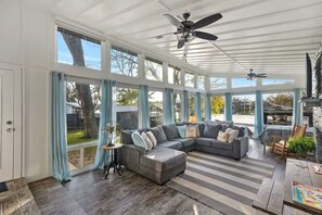 Relax in this spacious sunroom with a sofa, ottoman, and ceiling fan, offering a view of the outdoors through large windows.