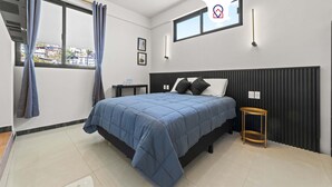 Ein modernes Schlafzimmer mit einem großen Bett, einem kleinen Nachttisch, einem Fenster mit Vorhängen und einer Wandleuchte.