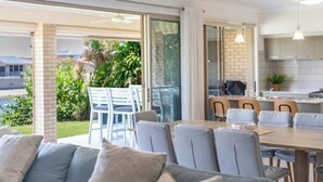 A modern dining area with a wooden table, grey upholstered chairs, and a glass door leading to an outdoor patio.