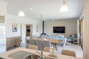 A modern kitchen with a dining area, a large TV, and a seating area with sofas and a coffee table.