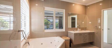 Une salle de bain moderne avec une baignoire, un meuble-lavabo et une fenêtre équipée de stores.