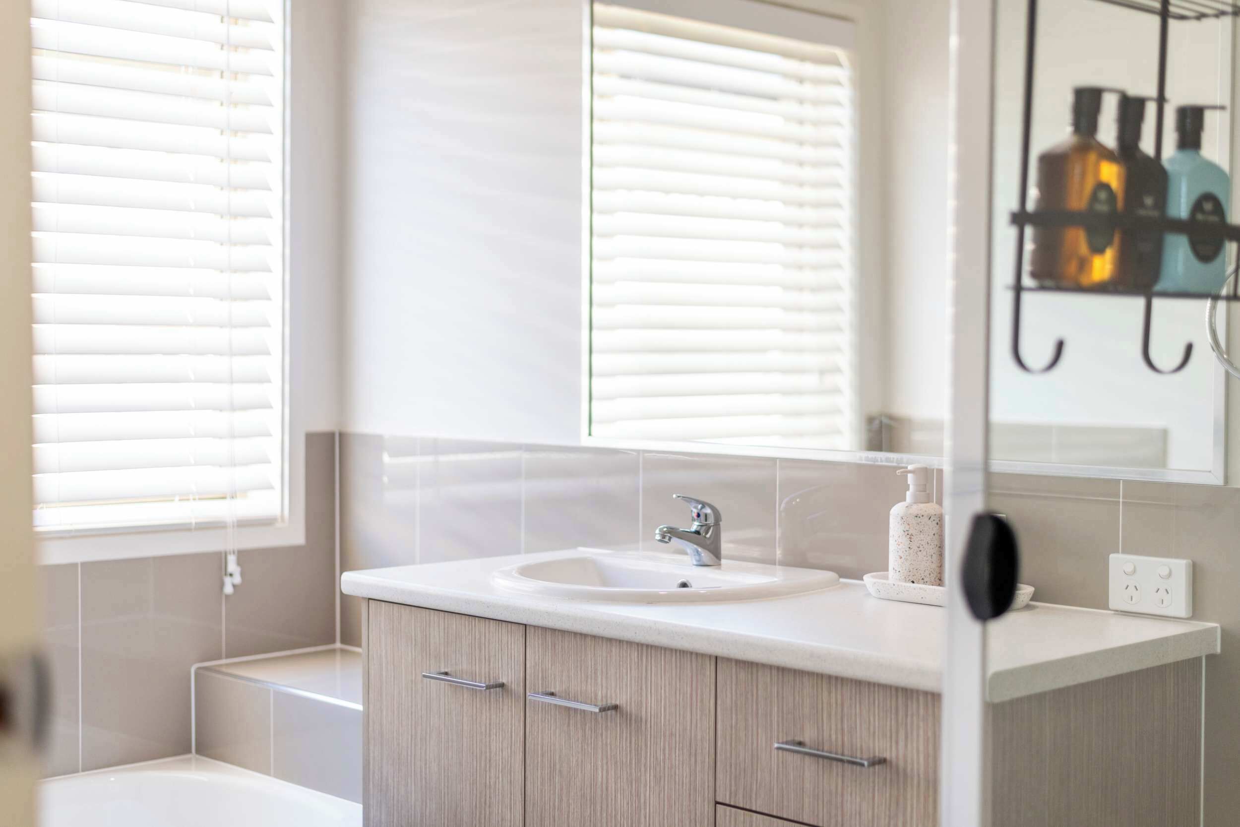 A bathroom with a sink, mirror, and window blinds.