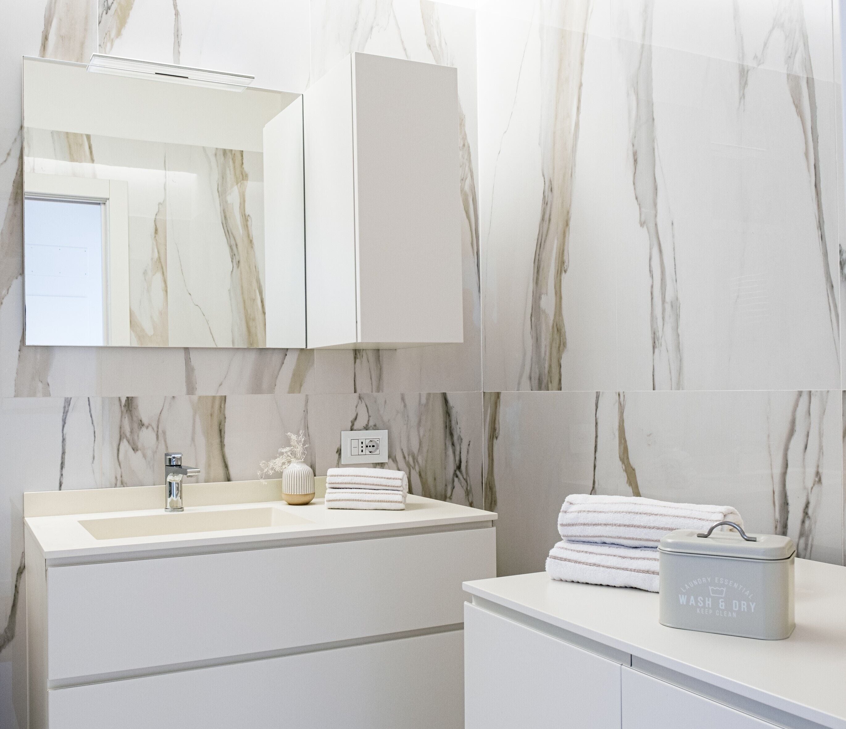 A modern bathroom with a marble backsplash, a sink, a mirror, and a towel rack.