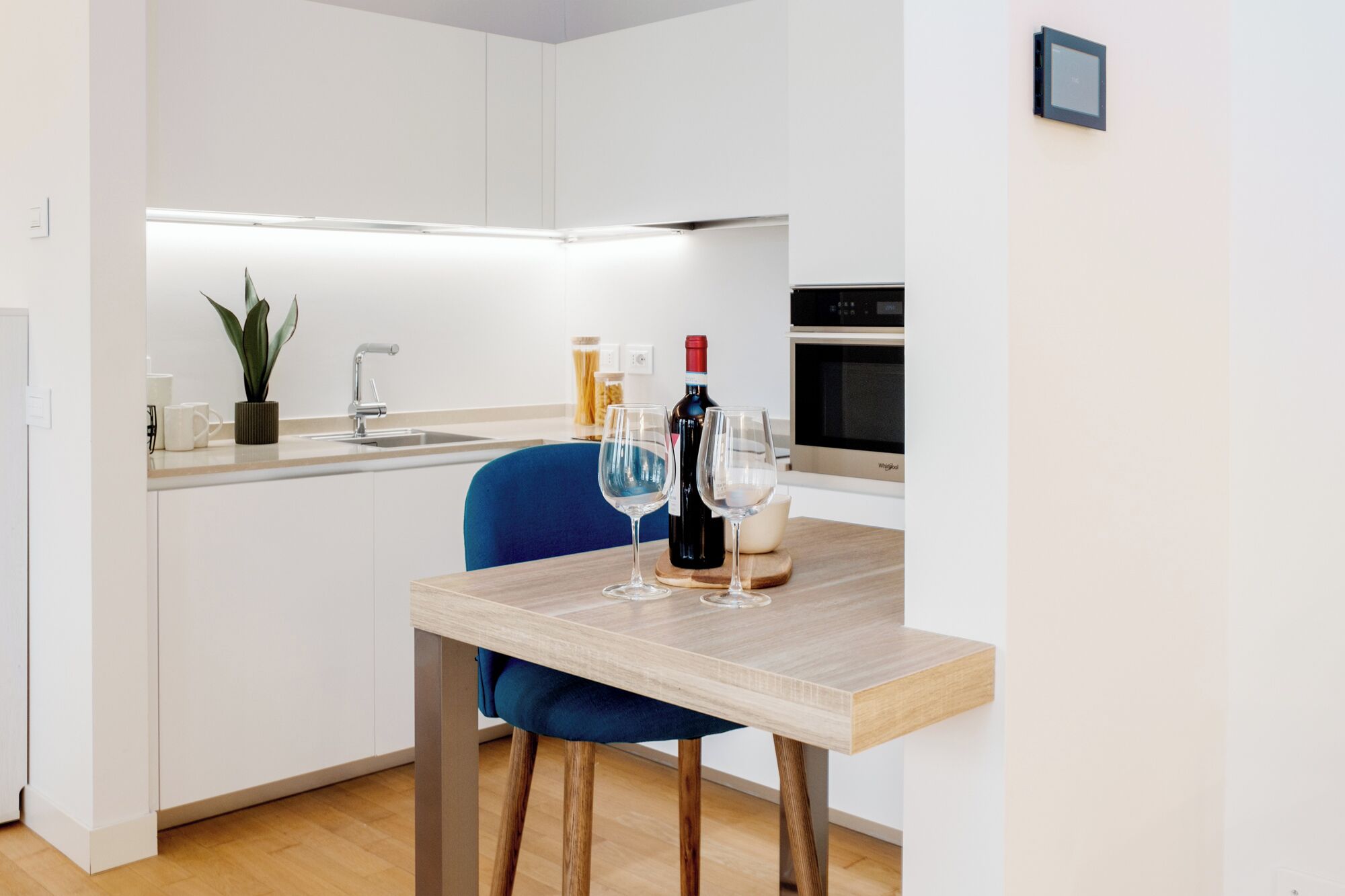 A compact kitchen with a dining area, featuring a sink, a stove, and a dining table with two wine glasses.