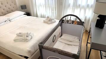 Une chambre d’hôtel avec un lit, un berceau, une table de chevet, une lampe et une fenêtre avec des rideaux.