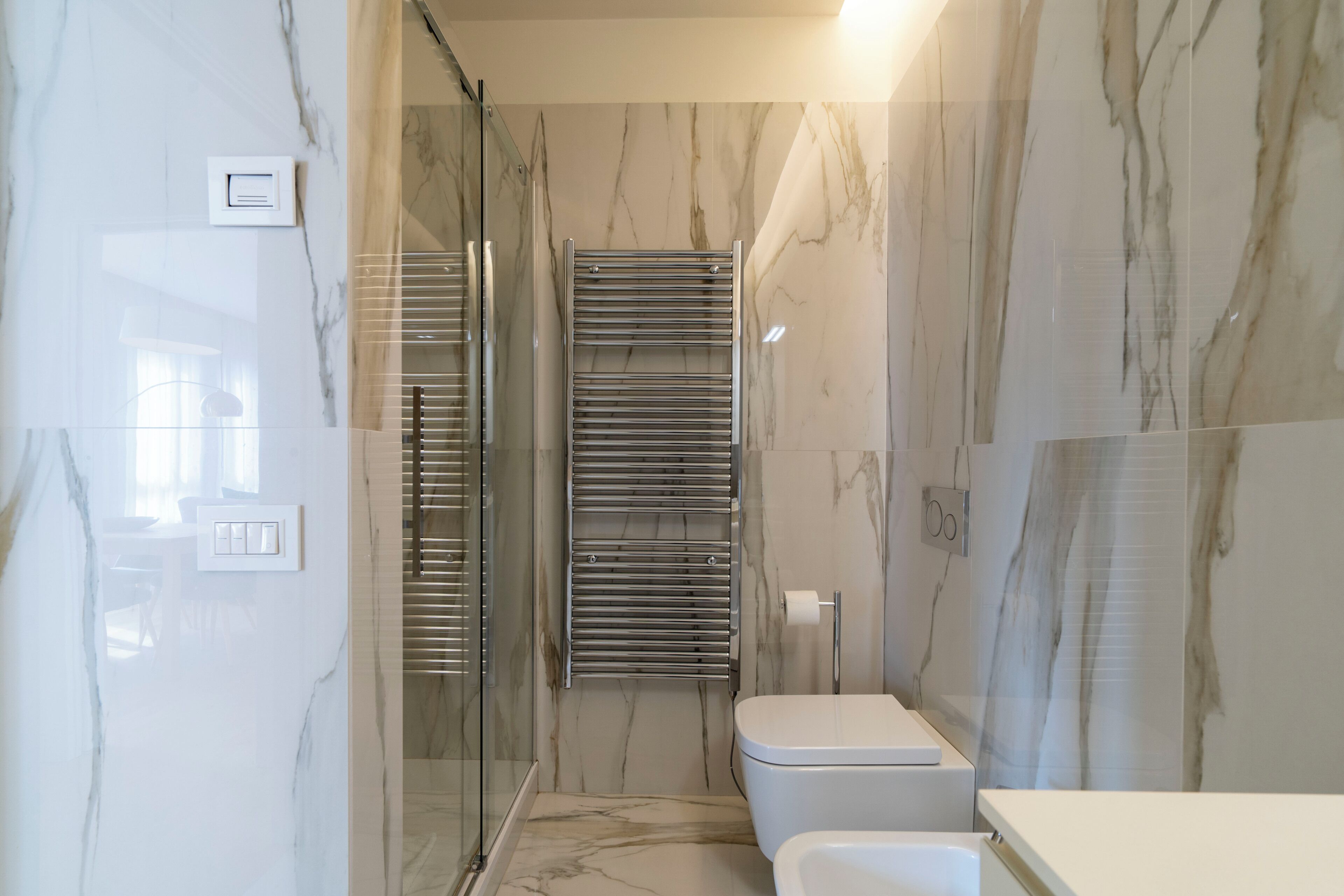 A bathroom with marble walls, a glass shower enclosure, a toilet, and a towel rack.