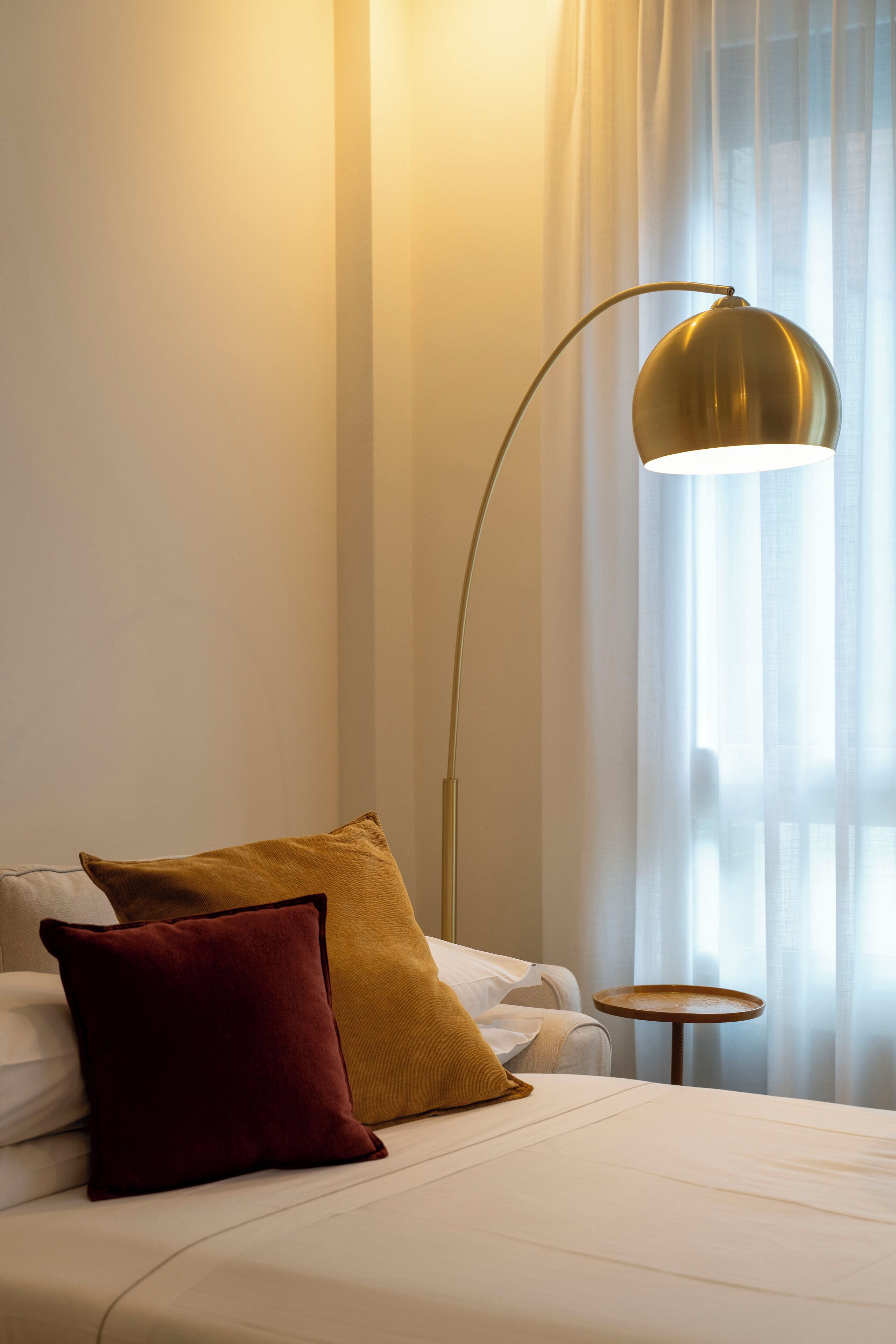Een hotelkamer met een bed, twee kussens, een ronde tafel en een vloerlamp.