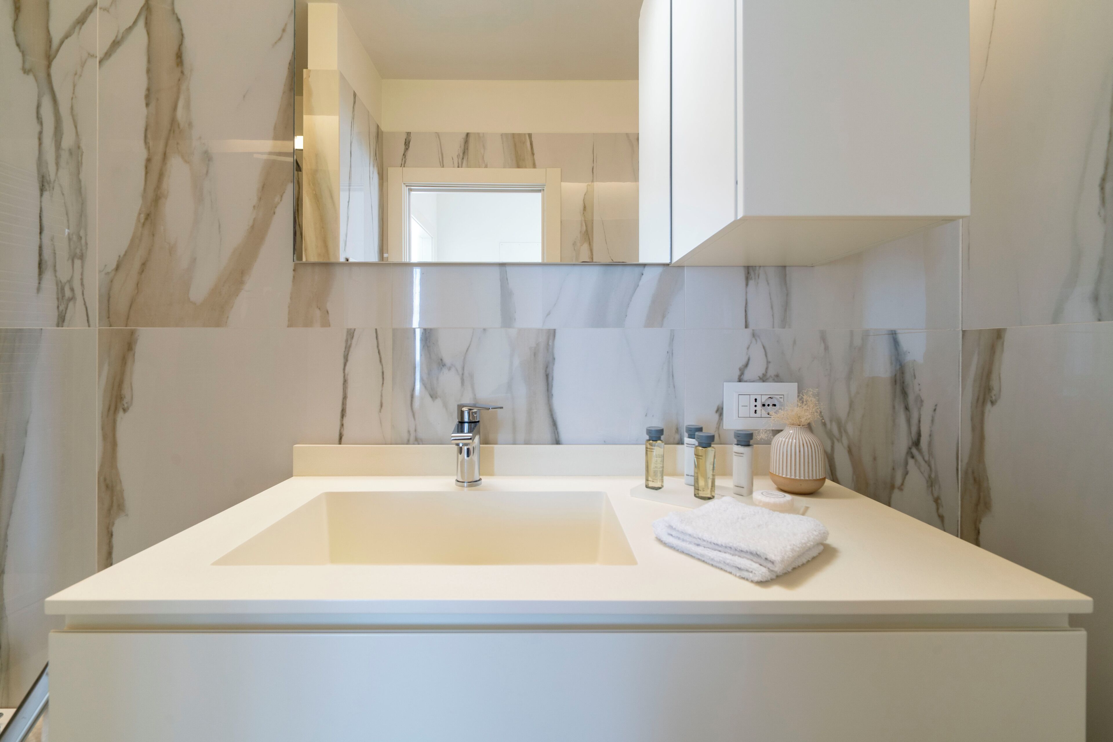 A modern bathroom with a marble sink, a mirror, and a towel.