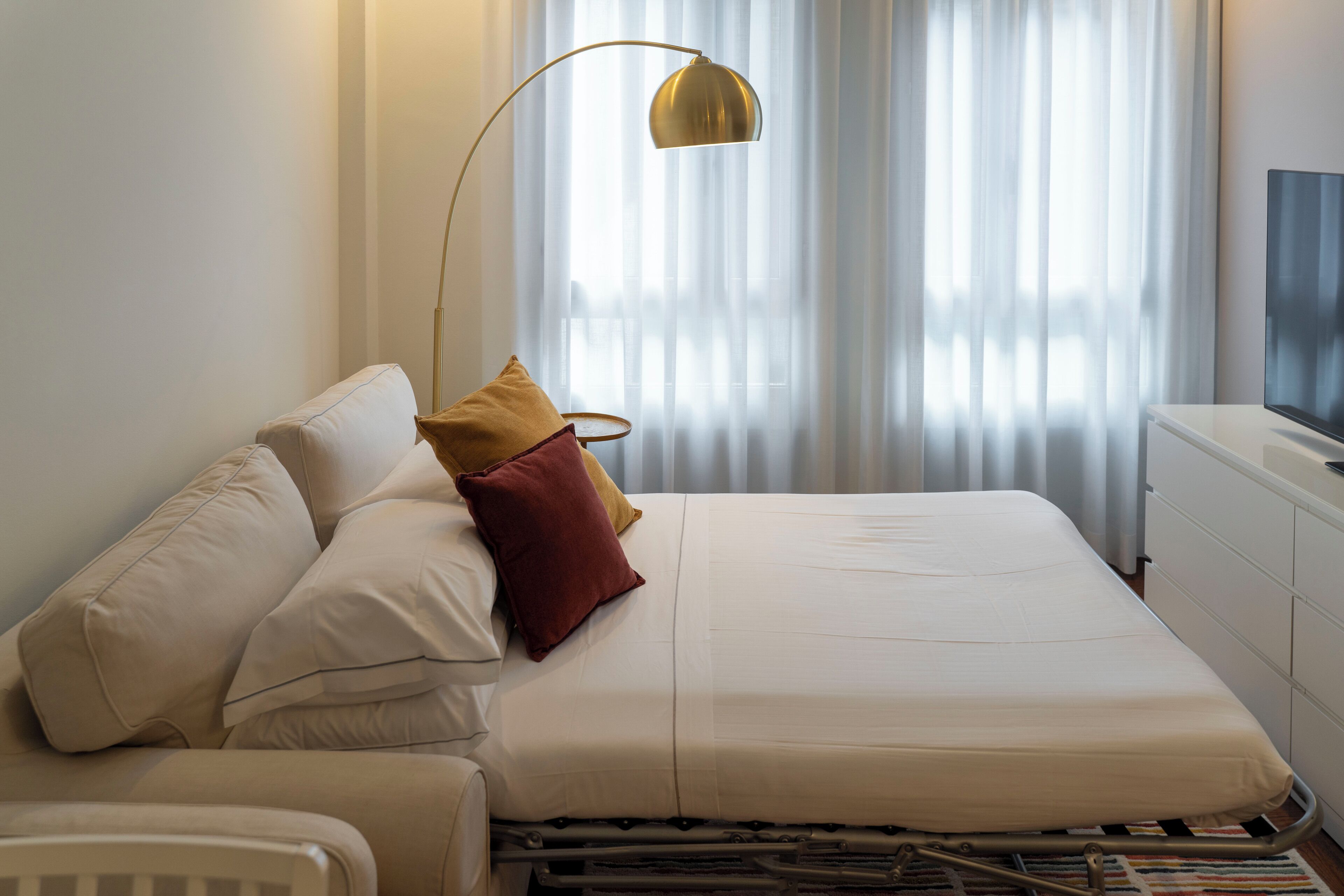 Een keurig opgemaakt hotelkamer met een bed, nachtkastje, televisie en een raam met gordijnen.