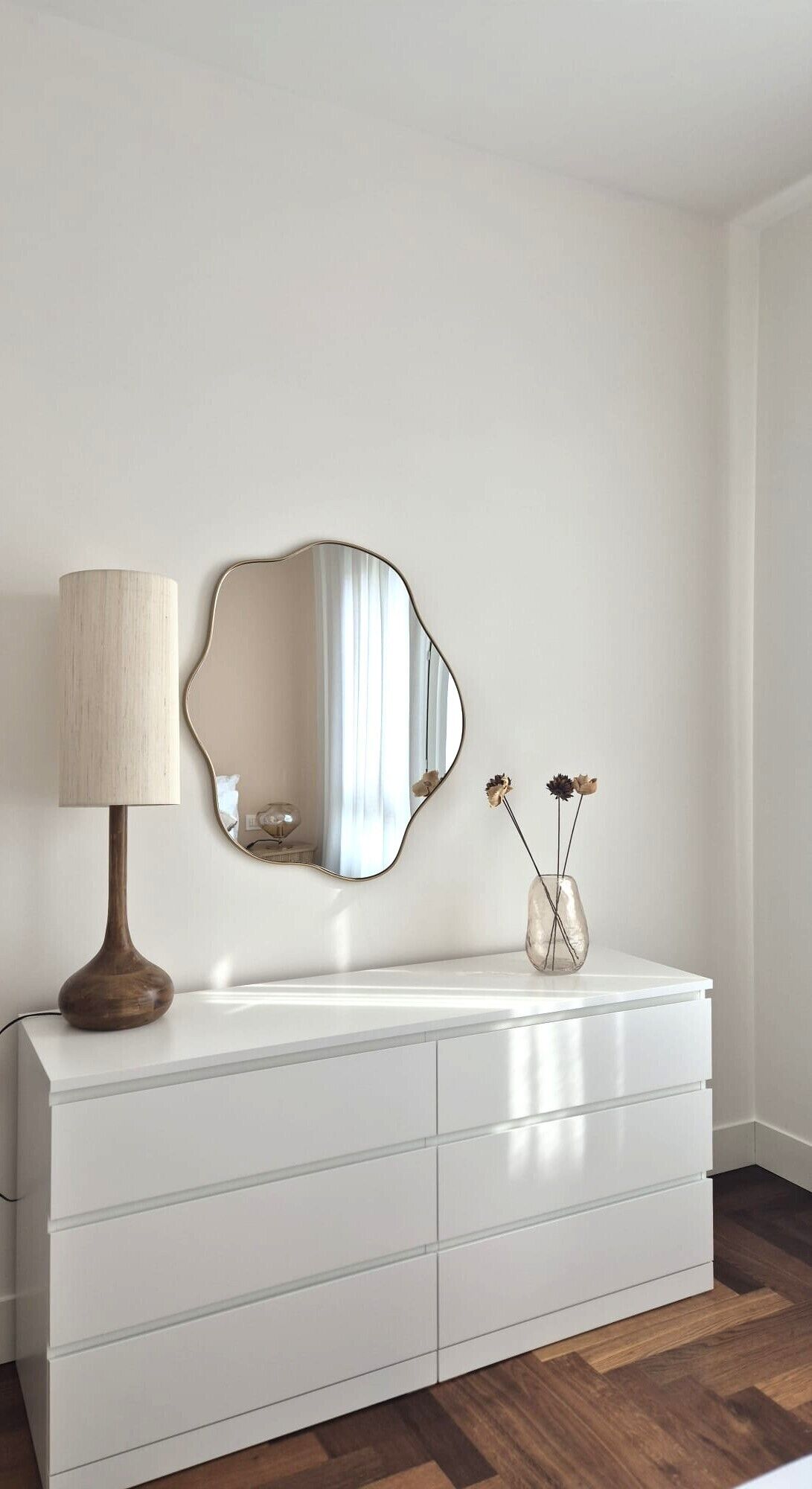 A white dresser with a mirror and a vase with dried flowers.