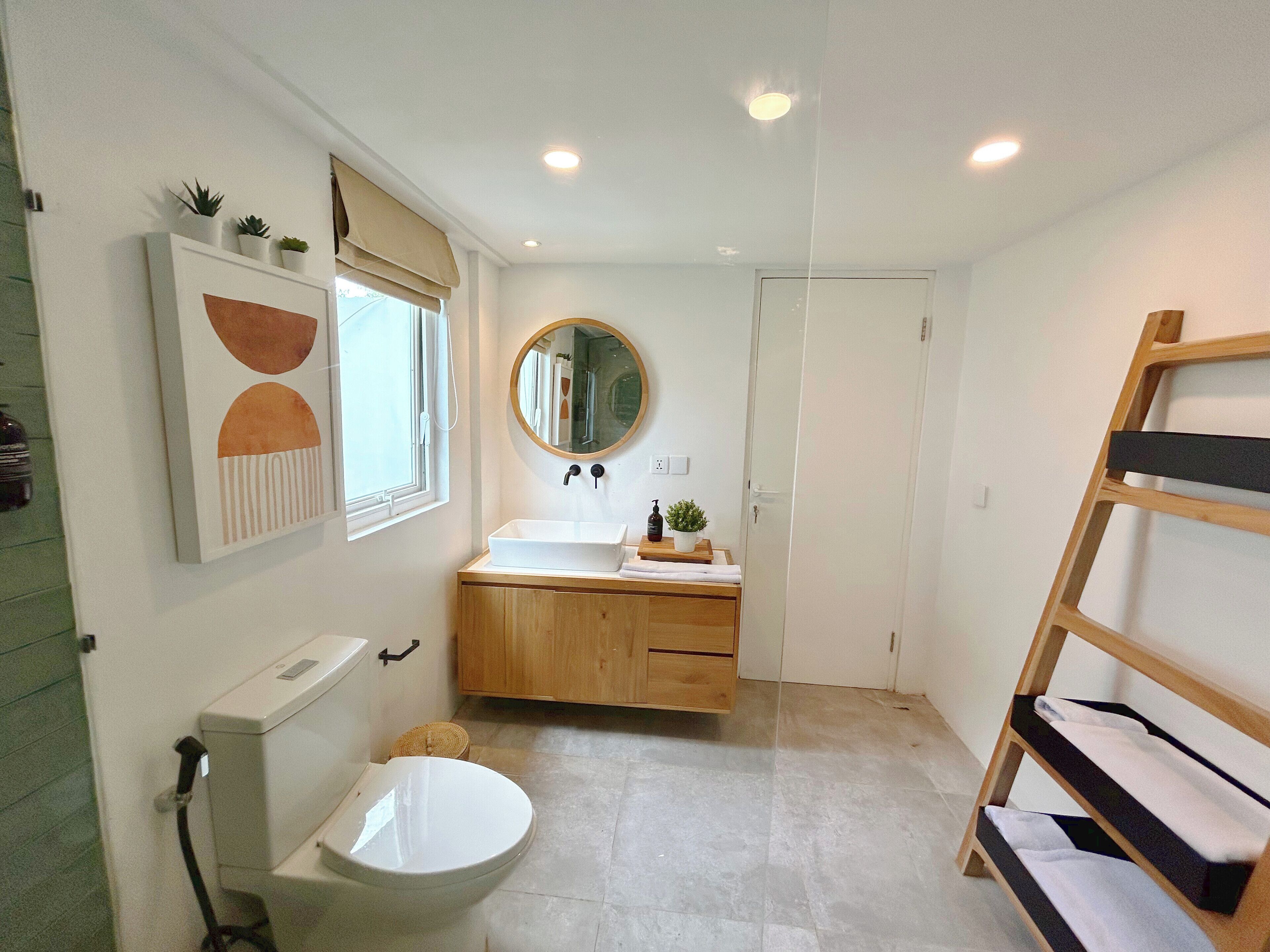 Un baño con inodoro, lavabo, espejo y estante de madera.