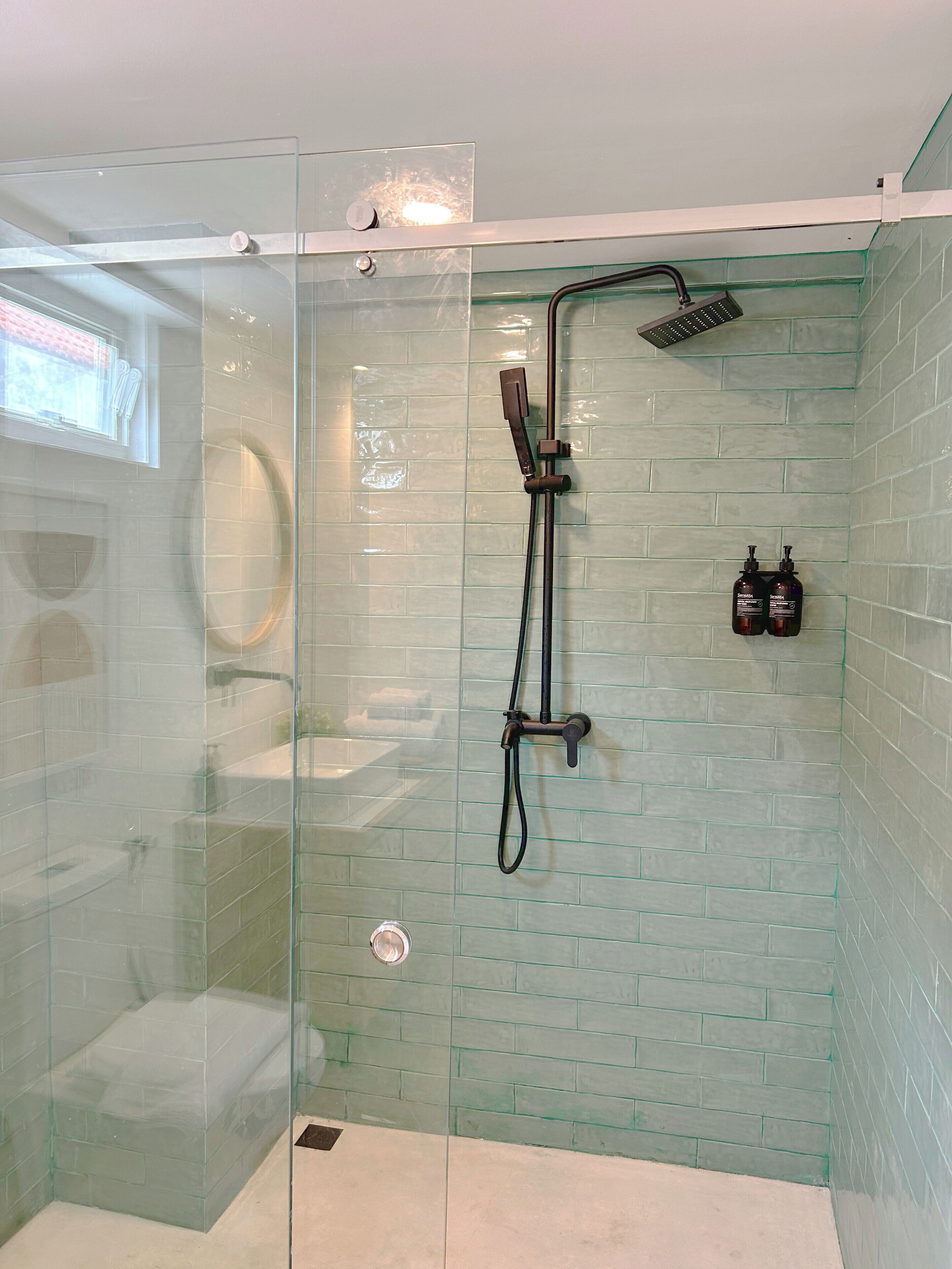 A glass-enclosed shower with a handheld showerhead and a wall-mounted faucet.
