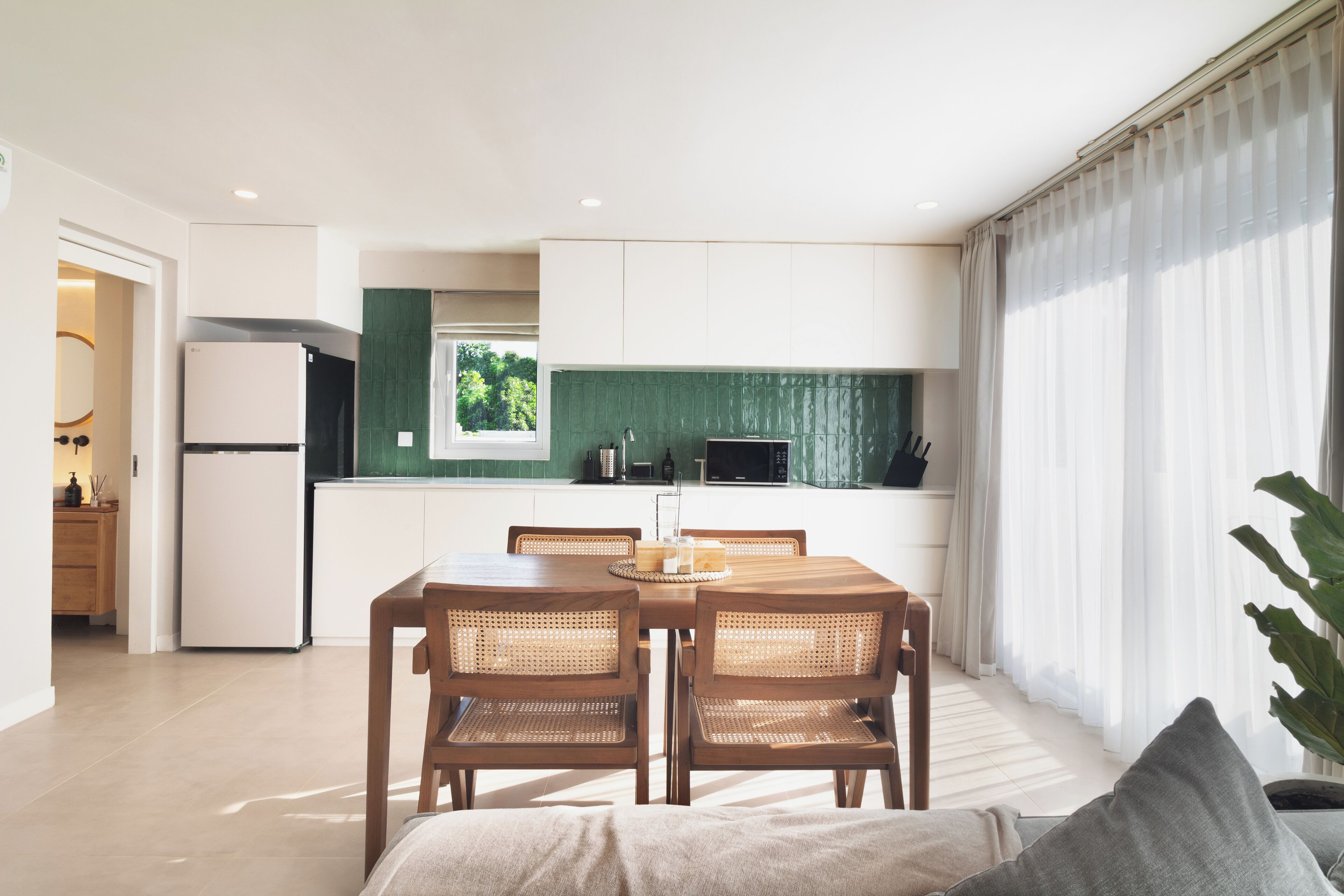 A modern kitchen with white cabinets, a green backsplash, and a dining area with a wooden table and chairs.