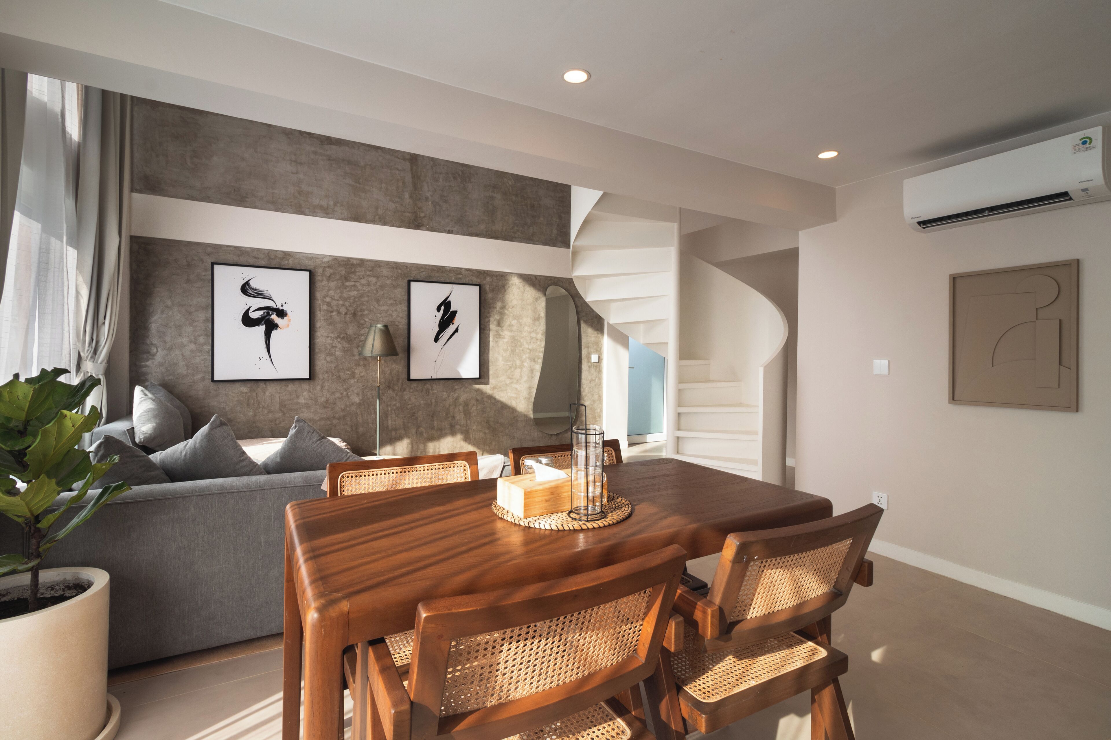 A modern dining area with a wooden table and chairs, a grey sofa, and abstract art on the walls.