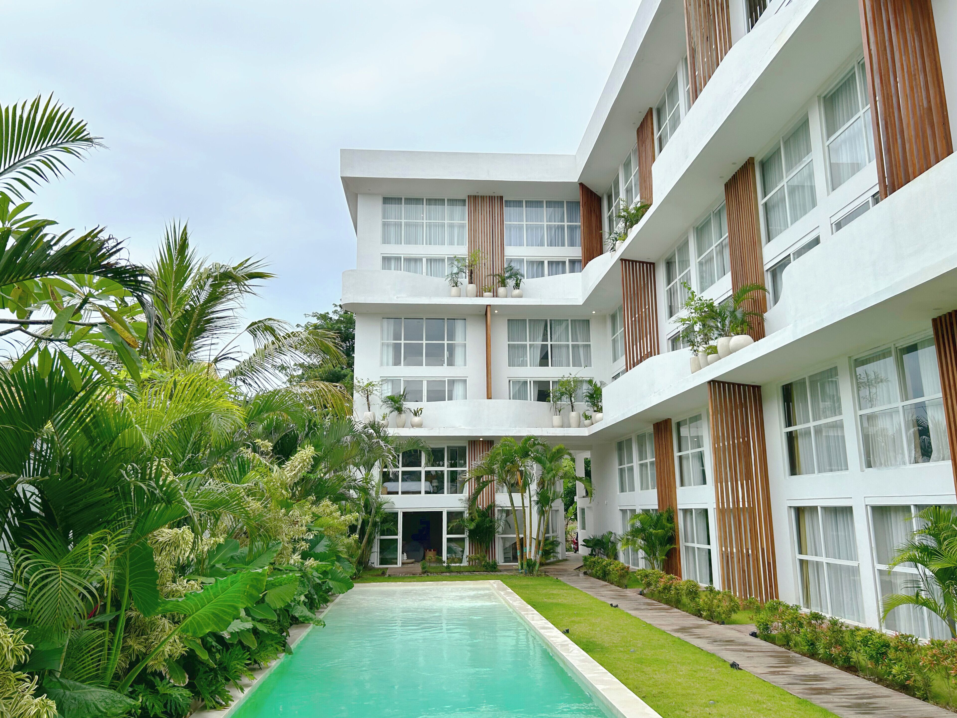 A modern multi-story building with a central courtyard featuring a swimming pool, surrounded by lush greenery and potted plants.