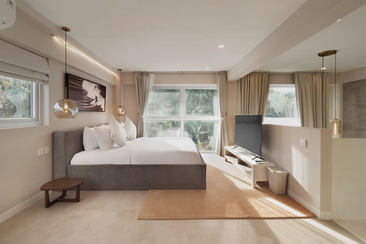 A modern bedroom with a large bed, a TV, a small table, and a window with curtains.