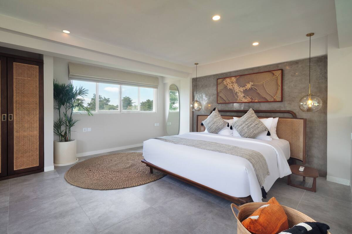 Een moderne slaapkamer met een groot bed, een potplant, een rond tapijt en uitzicht op de omgeving.