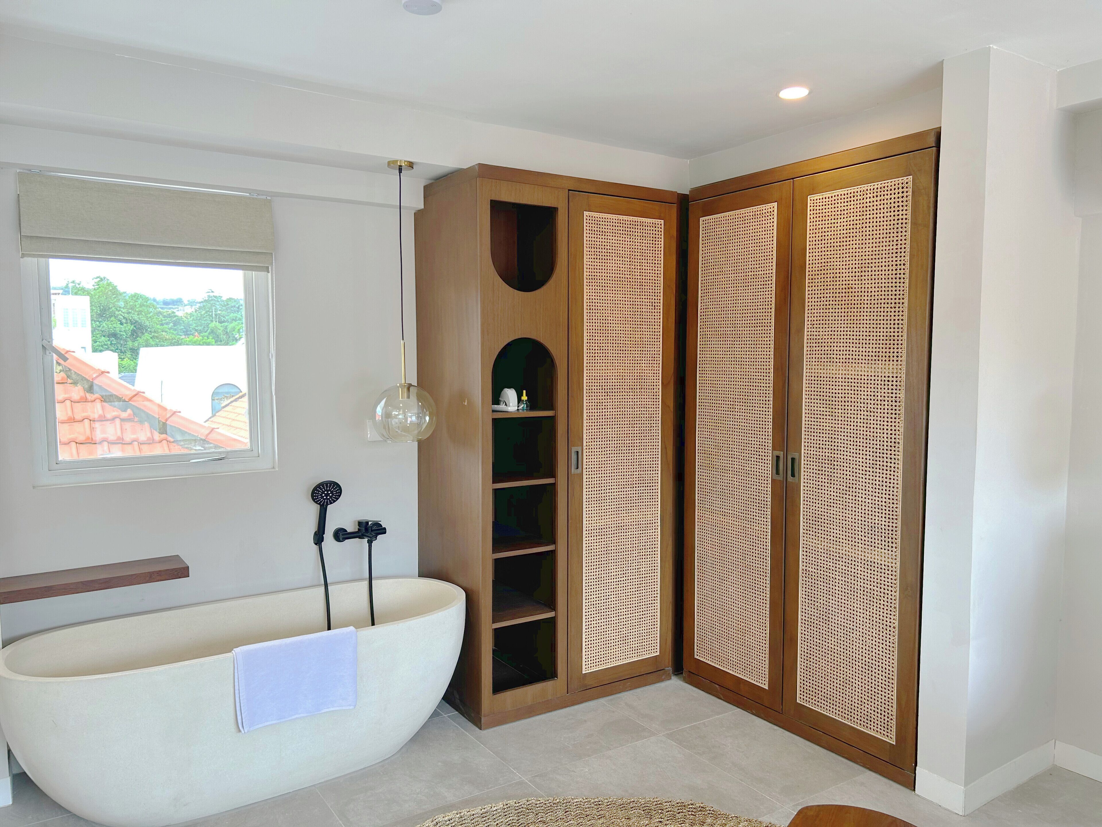 A modern bathroom with a freestanding bathtub, wooden wardrobe with a woven door, and a hanging light fixture.