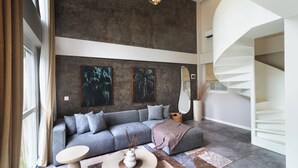 A modern living room with a grey sofa, a round coffee table, and a spiral staircase. - A.K.A Tropicana Bingin (Pecatu)